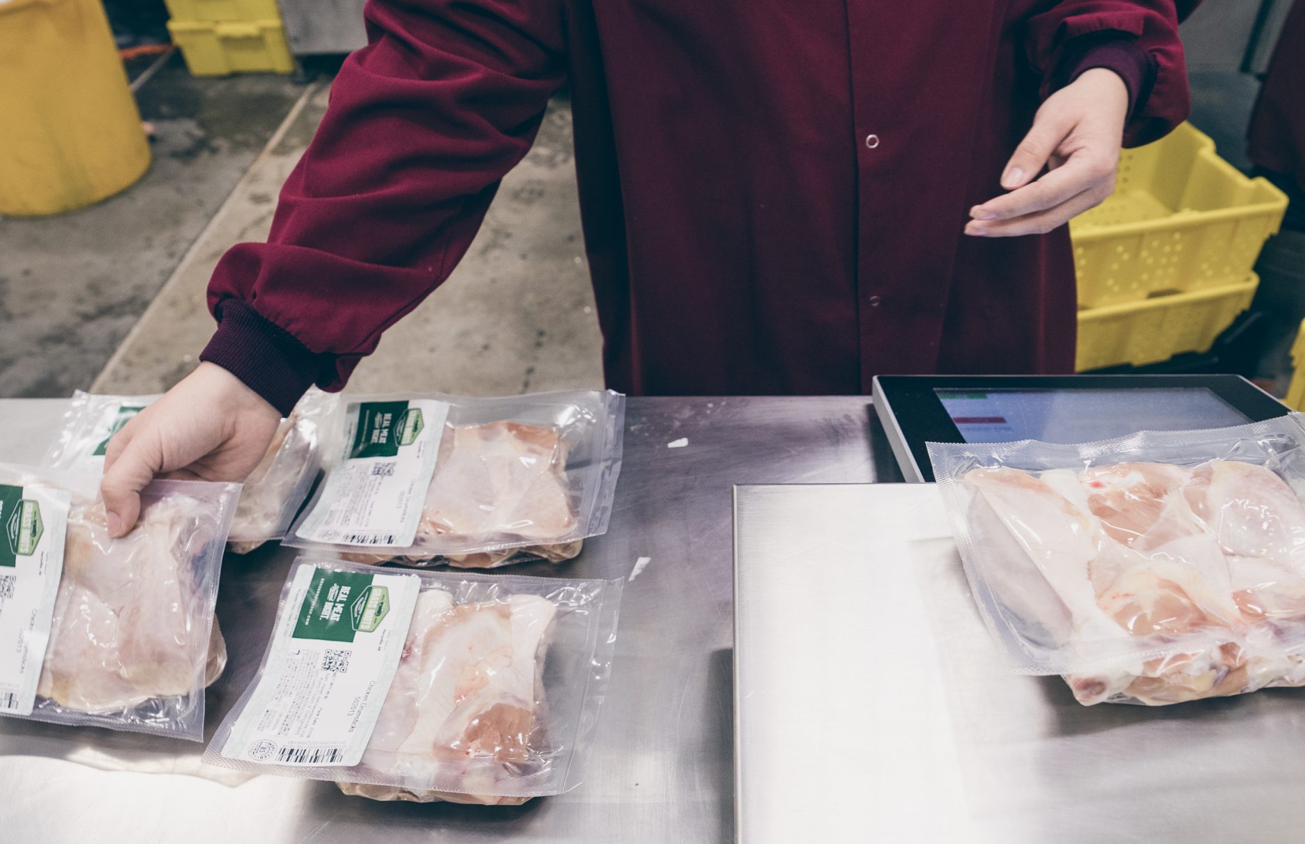 Shoulder down view of person wearing a maroon shirt packaging cuts of meats in plastic packages.